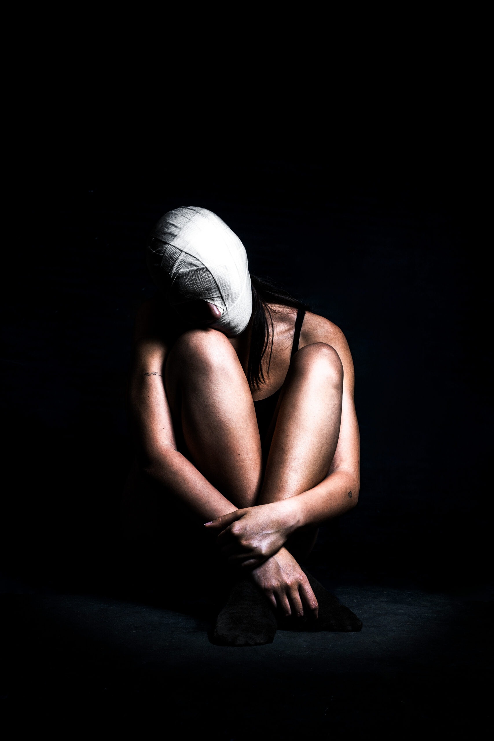 Ritratto di una ragazza con il corpo raccolto e il volto interamente ricoperto da bende bianche
